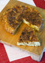 Food, Cooked, Eggs, Spanish omelette or tortilla on a wooden chopping board with a slice cut out.