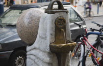 Austria, Vienna, Mariahilf Distrct, Drinking water fountain sponsored by C&A retail clothing company in street with parked car and bicycles behind.