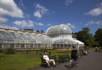 Ireland, Northern, Belfast, Botanic Gardens with people sat on benches outside the Palm House next to Queens University both designe by architect Charles Lanyon.