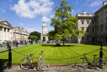 Ireland, County Dublin, Dublin City, Trinity College university with people walking through Parliament Square towards the Campanile with bicycles leaning against a chain fence in the foreground.