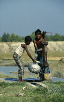 Bangladesh, Hatiya, Two boys drawing water from a UNICEF well into aluminium pitcher.