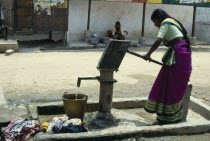 India, Andhra, Pradesh, Pochampally, Young woman drawing water at hand pump in street.