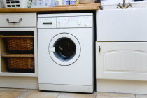 Architecture, Interiors, Machinery, White domestic washing machine household appliance set under worktop in utility laundry room.