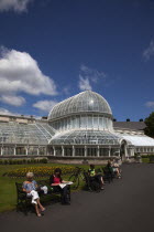 Ireland, Northern, Belfast, Botanic Gardens with people sat on benches outside the Palm House next to Queens University both designe by architect Charles Lanyon.