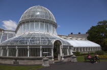 Ireland, Northern, Belfast, Botanic Gardens with people sat on benches outside the Palm House next to Queens University both designe by architect Charles Lanyon.