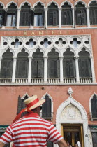 Italy, Veneto, Venice, Cropped shot of gondolier wearing red and white striped shirt and straw boater trimmed with red sash standing in front of facade of the Hotel Danieli.