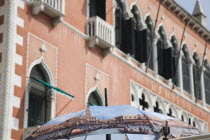 Italy, Veneto, Venice, Open umbrella printed with painting Return of the Bucentoro to the Molo on Ascension Day by Canaletto. Facade of the Hotel Danieli behind.