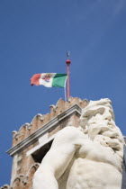 Italy, Veneto, Venice, Centro Storico, Arsenale, Part view of crenellated tower flying Italian tricolour flag with statue of Neptune in foreground against clear blue sky of late summer.