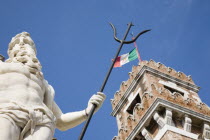Italy, Veneto, Venice, Centro Storico, Arsenale, Part view of crenellated tower flying Italian tricolour flag with statue of Neptune in foreground against clear blue sky of late summer.