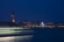 Italy, Veneto, Venice, Giudecca island, Early evening view towards illuminated Campanile of St. Mark with vaporetto water bus to Murano and Burano in blurred motion in foreground with light trails ref...