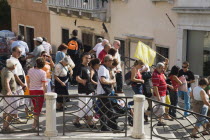 Italy, Veneto, Venice, Tour group of tourists crossing bridge in late summer led by guide holding flag above to show direction.