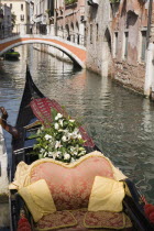 Italy, Veneto, Venice, Gondola prepared for wedding with flowers and red and gold brocade seating moored at canal jetty.