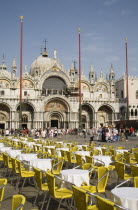 Italy, Veneto, Venice, Centro Storico, St. Marks Square,  Cafe tables prepared for customers in early morning sunshine with facade of Basilica di San Marco behind.