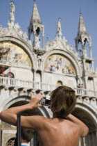 Italy, Veneto, Venice, Centro Storico, St. Marks Square, Tanned female tourist wearing backless top taking photograph of Basilica di San Marco.