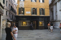Italy, Veneto, Venice, Centro Storico, Cartier jewellery store exterior with security guard and tourists in paved square, with shuttered facade and plaque depicting St George and the dragon.