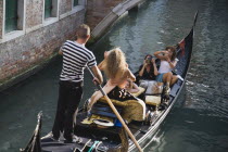 Italy, Veneto, Venice, Centro Storico, Gondolier steering gondola along canal as models are photographed for fashion shot in late summer sunshine.