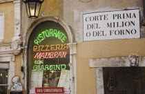 Italy, Veneto, Venice, Centro Storico, Pizzeria window in old city wall with neon advertising, menus and sign for air conditioning. Painted street sign on wall at side above doorway.