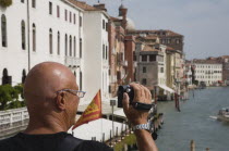 Italy, Veneto, Venice, Male tourist making a video recording from bridge looking along canal in late summer sunshine.