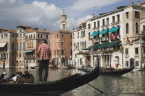 Italy, Veneto, Venice, Gondolier manoeuvres gondola before start of Regata Storico the Venice annual historical Regatta in September. Canalside buildings behind.