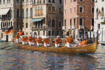 Italy, Veneto, Venice, Grand Canal, Regatta Storico historical annual regatta. Team of rowers wearing orange and white costume passing canalside buildings with onlookers watching from balconies.