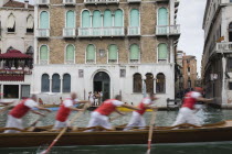 Italy, Veneto, Venice, Grand Canal, Participants in the Regata Storico historical Regatta held annually in September in blur of motion as they approach the Rialto bridge passing canalside buildings wi...