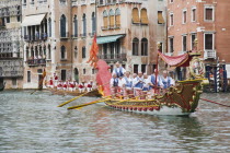 Italy, Veneto, Venice, Grand Canal, Participants in the Regata Storico, historical regatta held annually in September in red and gold decorated gondola and wearing traditional costume approaching the...