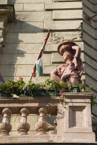 Hungary, Pest County, Budapest, Art Nouveau exterior facade with rolled Hungarian flag, flower pots and statue on stone balcony.