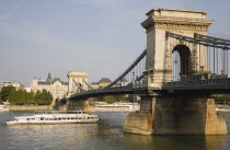 Hungary, Pest County, Budapest, Szechenyi Chain Bridge or Memory Bridge from Buda with pleasure boat on the River Danube below.