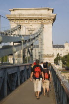 Hungary, Pest County, Budapest, tourists with matching day packs crossing Szechenyi Chain Bridge or Memory Bridge over the River Danube on foot.