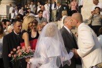 Hungary, Pest County, Budapest, bride and groom greeting wedding guests on steps of Saint Stephens Basilica with groom leaning forward to kiss older man on cheek.