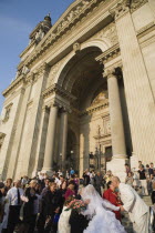 Hungary, Pest County, Budapest, bride and groom greeting wedding guests on the steps of Saint Stephens Basilica after service, both leaning forward to kiss older couple on cheek.