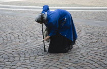 Hungary, Pest County, Budapest, elderly woman bent over and supported with cane begging in square in front of Saint Stephen Basilica.