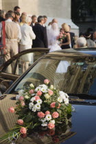 Hungary, Pest County, Budapest, bride and groom greeting wedding guests on steps of Saint Stephens Basilica with bouquet laid on bonnet of car in foreground.
