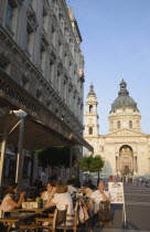 Hungary, Pest County, Budapest, cafe with Summer tourists seated at outside tables with Saint Stephens Basilica behind.