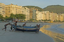 BRAZIL Rio de Janeiro Launching a fishing boat at Copacabana beach at daybreak, fishermen and a few early-morning walkers on the beach, soft sunlight on the hotel facades.