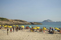 BRAZIL Rio de Janeiro Arpoador end of Ipanema beach yellow umbrellas blue sea and sky, swimmers in sea and on rocks and pigeons on beach.