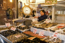 Chile, Santiago, Mecardo Central, Shellfish fresh fish and octopus on sale with prices clearly displayed, Vendor behind counter by a large clock and weighing scale, With a 5 million ton annual catch t...