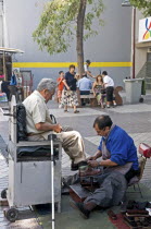 Chile, Santiago, Shoe-shine in downtown shopping area, disabled man with crutch against chair, shoe brushes.