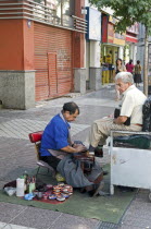 Chile, Santiago, Shoe shine in downtown shopping area, piles of shoe polish tins.