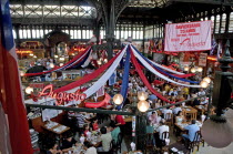 Chile, Santiago, Seafood restaurant section of Central Market with diners eating at tables under red white and blue hanging decorations, the ironwork used in the structure of the building which was co...