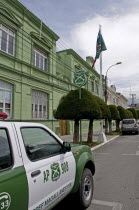 Chile, Magallanes, Punta Arenas, green painted Police Headquarters off the Plaza Munoz Gamero with a green and white police car parked outside and the crossed rifles logo of the Carabineros de Chile v...
