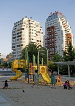 Chile, Santiago, Children playing in the sand while thier mothers watch at a playground in Plaza Peru in Vitacura Santiago's plushest neighbourhood, highrise apartment blocks.