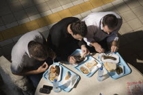 Hungary, Pest County, Budapest, looking down on three young men seated at circular table having lunchtime meal of Hungarian sausages, bread and pickles at the Central Market Nagy Vasarcsarnok. Mobile...