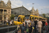 Hungary, Pest County, Budapest, trams and crowd of passengers in front of rail terminus Budapest Nyugati palyaudvar and walking down steps to metro in foreground. Man appears to be begging on right ha...