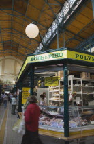 Hungary, Pest County, Budapest, stall selling Hungarian sausages, hams, bacon, and other meats at Nagy Vasarcsarnok, the indoor Central Market. Woman carrying shopping bags walks past in foreground.