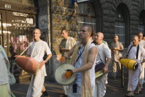 Hungary, Pest County, Budapest, Hare Krishna devotees singing and dancing on Andrassy UtIn Pest with graffiti covered doorway behind. The International Society for Krishna Consciousness or ISKCON, als...