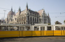 Hungary, Pest County, Budapest, yellow tram passing the Parliament Building.