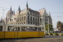 Hungary, Pest County, Budapest, yellow tram passing the  Parliament Building.