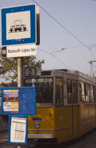 Hungary, Pest County, Budapest, yellow tram approaching stop and signpost displaying timetable.