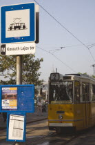 Hungary, Pest County, Budapest, yellow tram approaching stop and signpost displaying timetable.